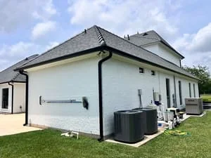 Black seamless gutters and downspout system installed on white residential home with dark roof
