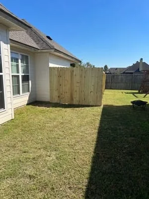 Newly installed pressure-treated wood fence along residential property with manicured lawn