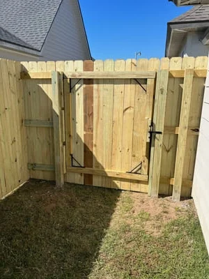 Newly installed pressure-treated wood privacy fence with gate in residential backyard