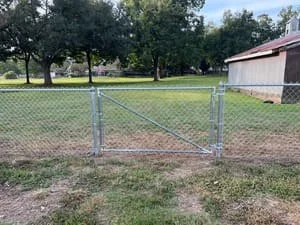 Galvanized chain-link fence with gate installed along property line with concrete posts