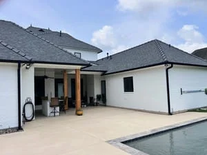 Black gutters and downspouts on white modern home with dark roof and patio